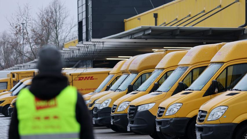 Am Zustellstützpunkt der Deutschen Post DHL am Hauptbahnhof in Rostock haben sich Mitarbeiter zum Warnstreik eingefunden, im Hintergrund stehen die Zustellfahrzeuge.