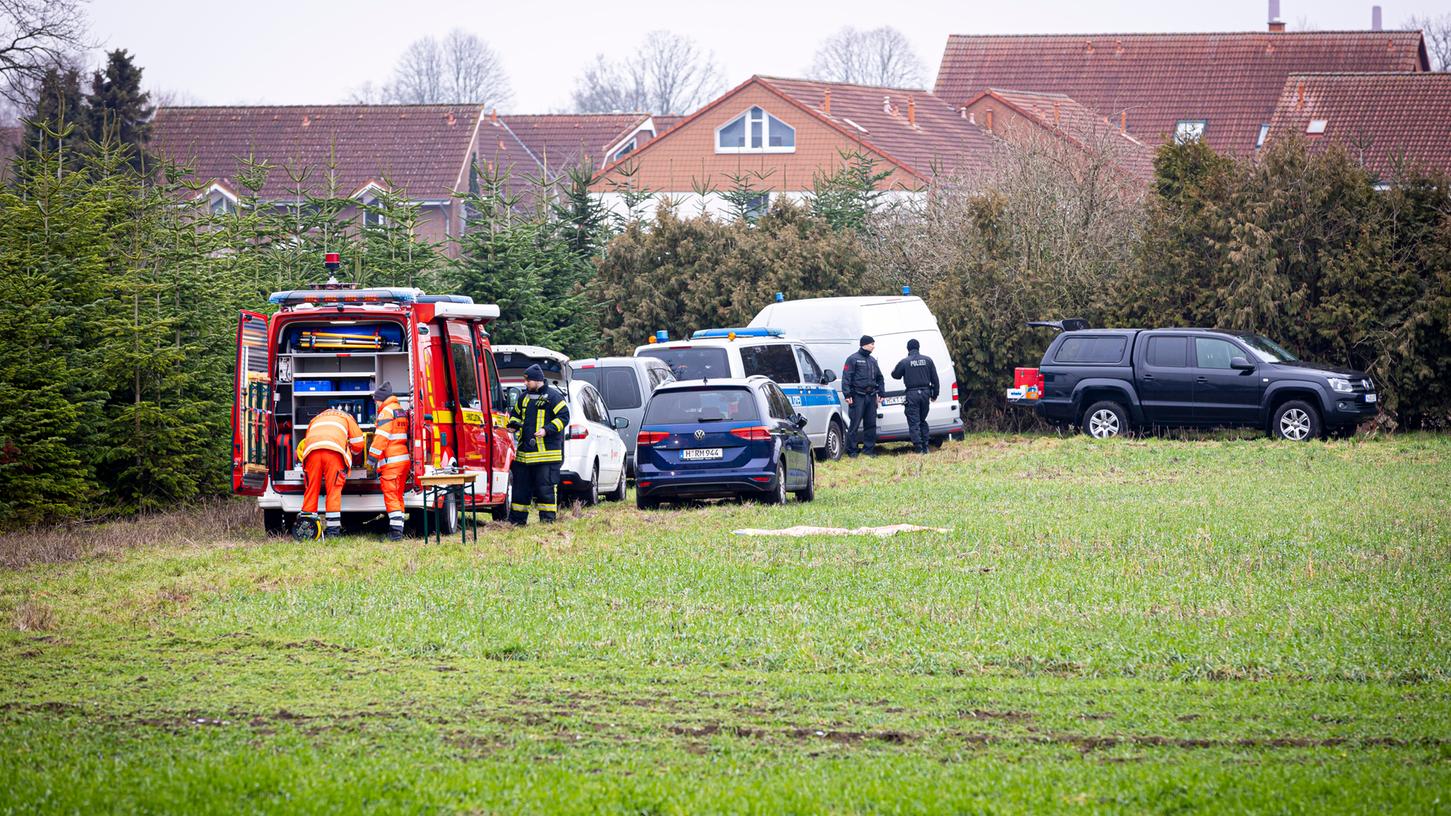 Einsatzkräfte von Polizei und Feuerwehr stehen auf einer Wiese. Auf der Suche nach einer mutmaßlich getöteten Person haben Einsatzkräfte am Vormittag auch ein Waldgebiet im niedersächsischen Wunstorf durchkämmt.