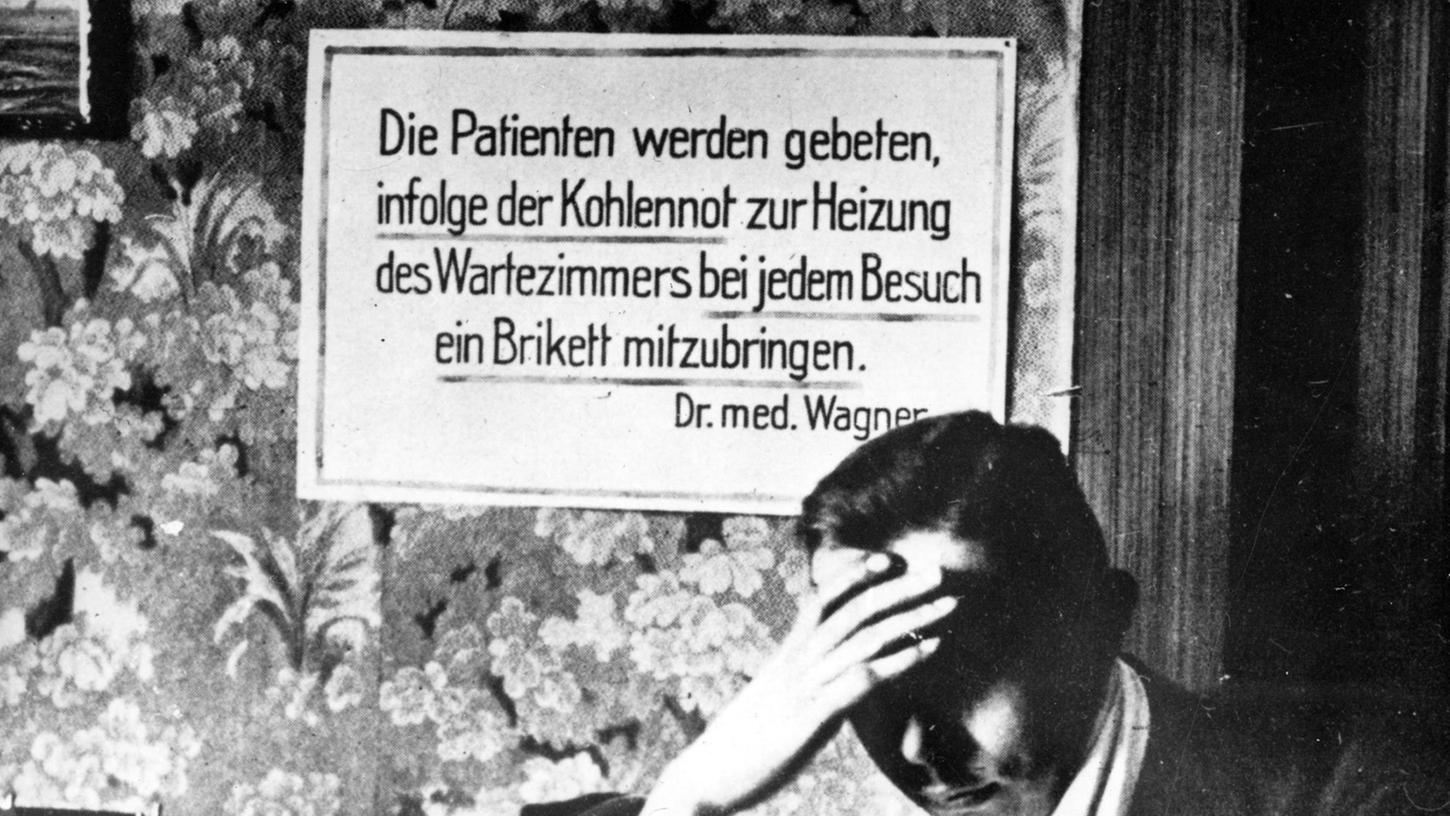 Das Archivbild von 1923 zeigt ein Schild und einen sitzenden Mann in einem Wartezimmer des deutschen Arztes Dr.med.Wagner. Aufgrund der Kohlenknappheit während der Inflation im Jahr 1923 wurden die Patienten gebeten, bei ihrem Besuch ein Brikett mitzubringen, um das Wartezimmer zu heizen. 