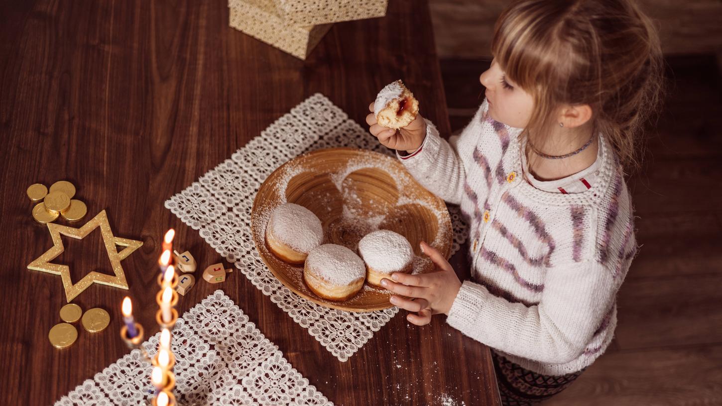 Eine Familie feiert den vielleicht bekanntesten jüdischen Feiertag, Chanukka. Dabei sind Sufganijot, meist warm gegessene Krapfen, eine typische Speise.