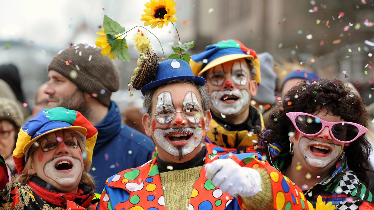Besucher in Clown-Kostümen werfen in Nürnberg beim Faschingsumzug mit Konfetti.