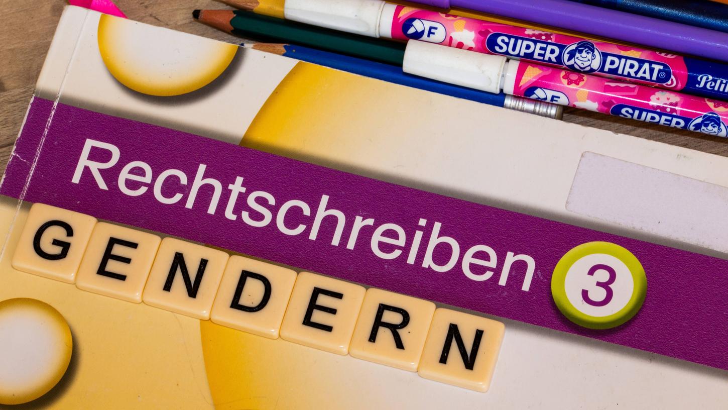 Buchstabenwürfel auf einem Schulbuch zeigen das Wort "Gendern". (Symbolbild) 