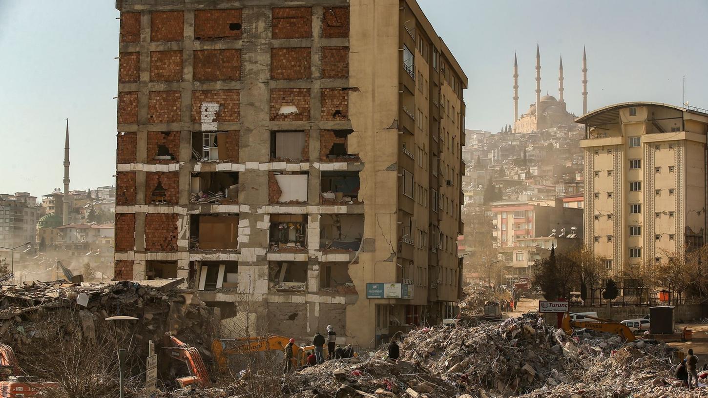 Menschen stehen im türkischen Kahramanmaras vor einem eingestürzten Gebäude. Menschen stehen im türkischen Kahramanmaras vor einem eingestürzten Gebäude.