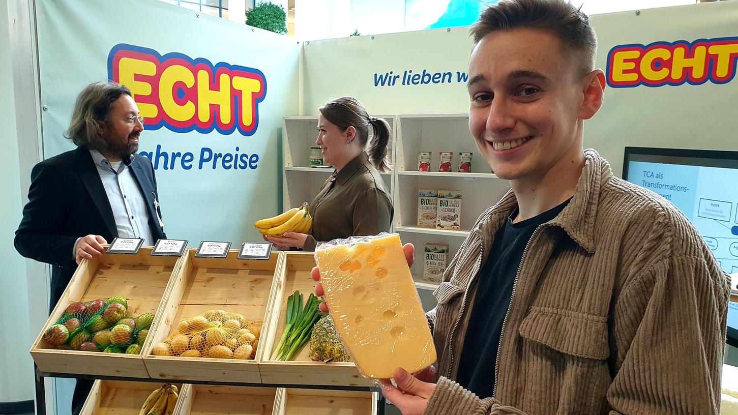 Lennart Stein präsentiert Käse im Supermarkt der wahren Preise mit Professor Tobias Gaugler und Studentin Viktoria Vogel.