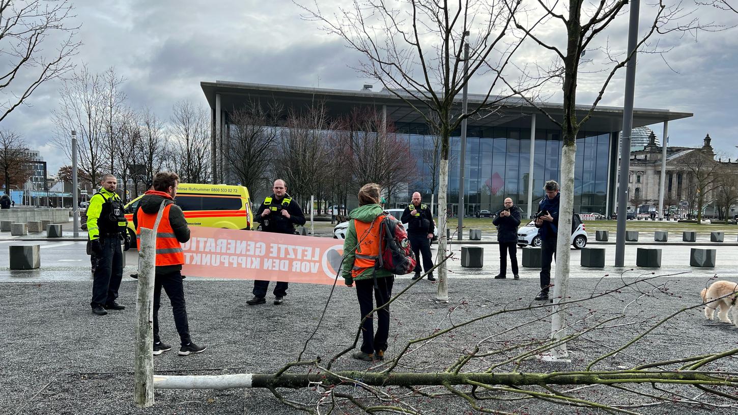Klimaschutz-Demonstranten stehen vor einem gefällten Baum mit dem Rücken zum Bundeskanzleramt.