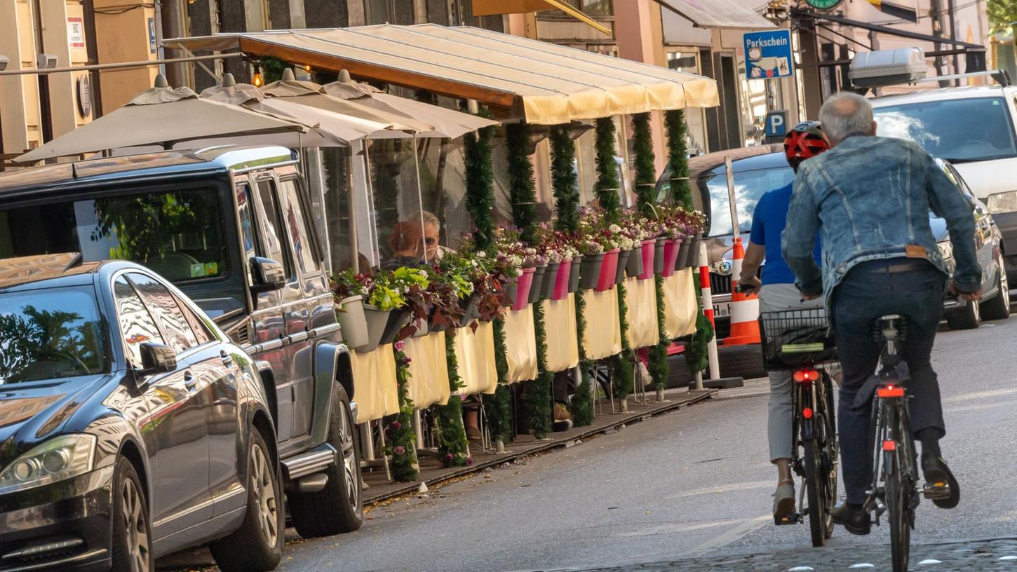 Zwei "Schanigärten" stehen in München auf dem Parkplatzbereich einer Straße.