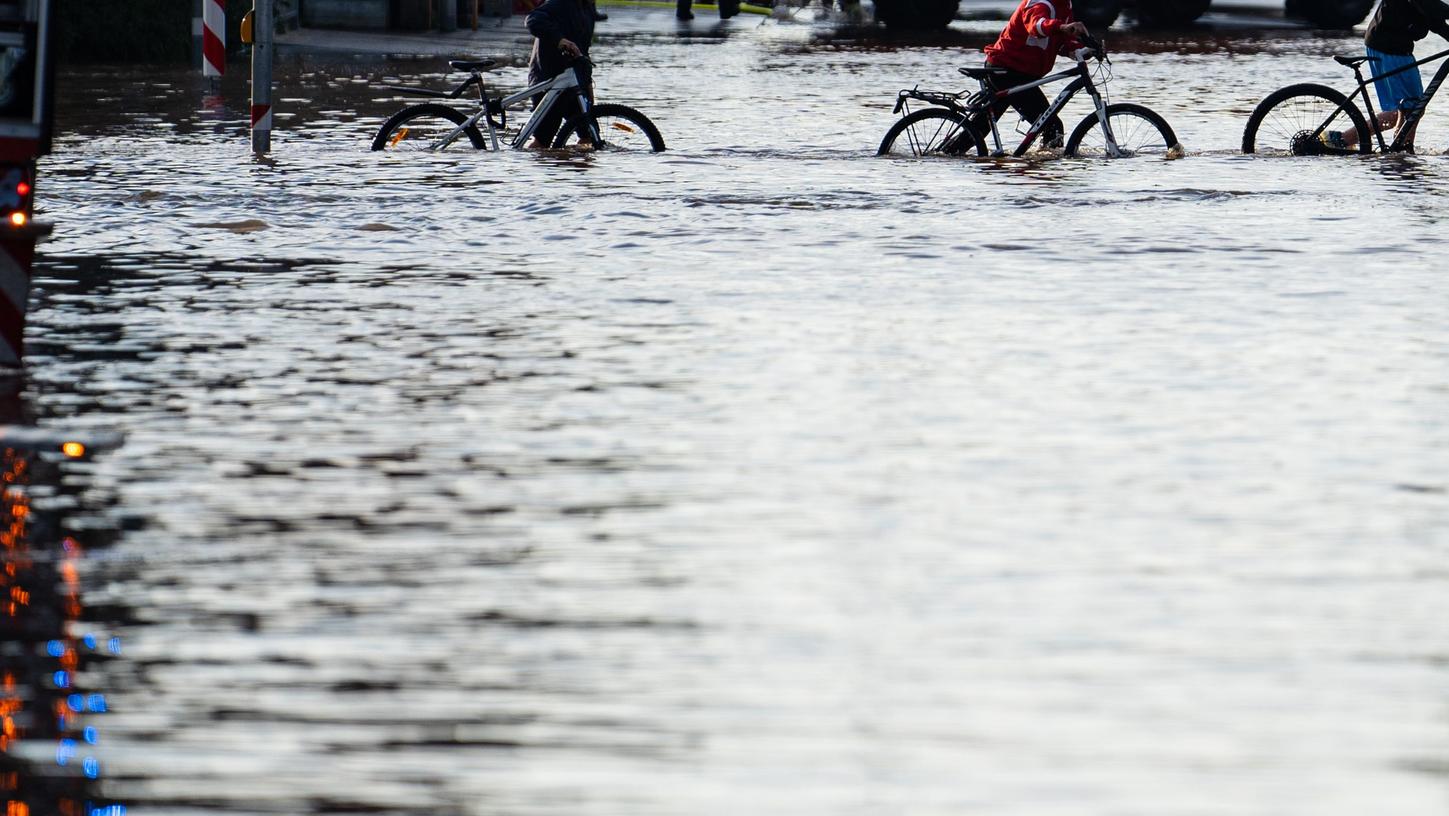 Jugendliche schieben ihre Fahrräder über eine überschwemmte Kreuzung.