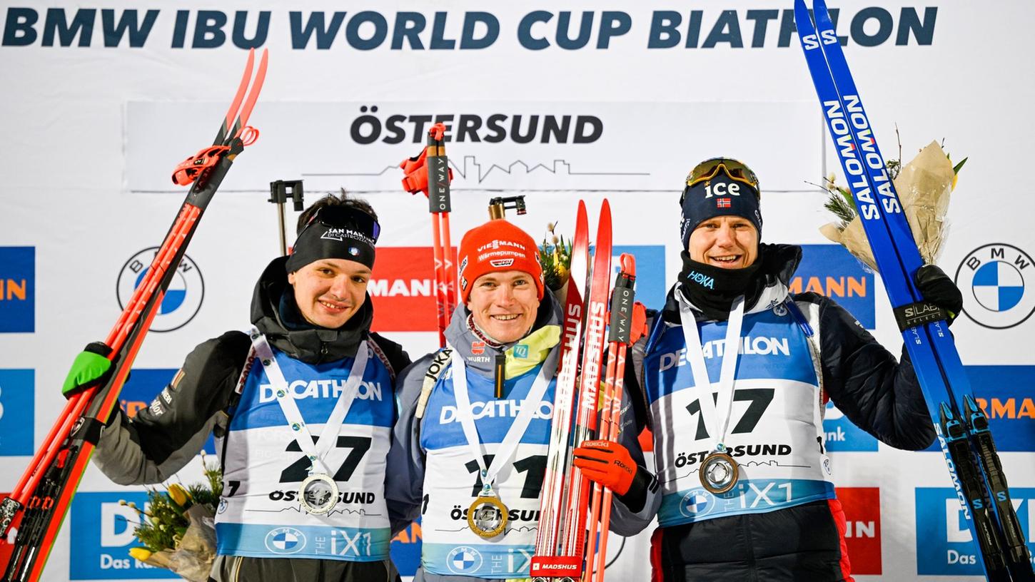 Benedikt Doll (M) feiert auf dem Podium seinen Sieg. Daneben: Tommaso Giacomel (l), Zweitplatzierter aus Italien, und Vetle Sjastad Christiansen, Drittplatzierter aus Schweden.