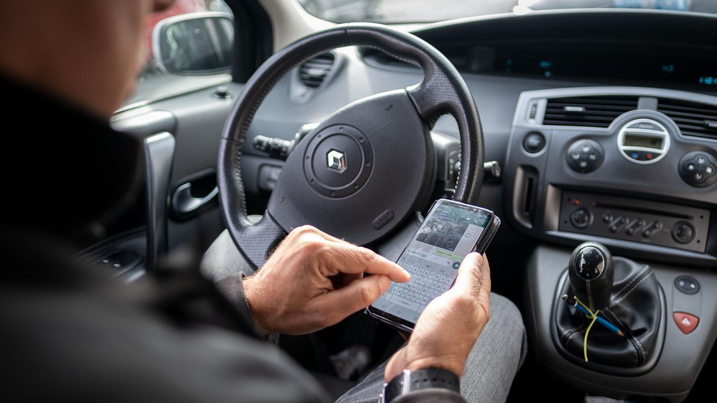 Ein Mann schreibt im Auto auf einem Smartphone eine Nachricht. Dafür kann er eine teure Strafe erhalten.