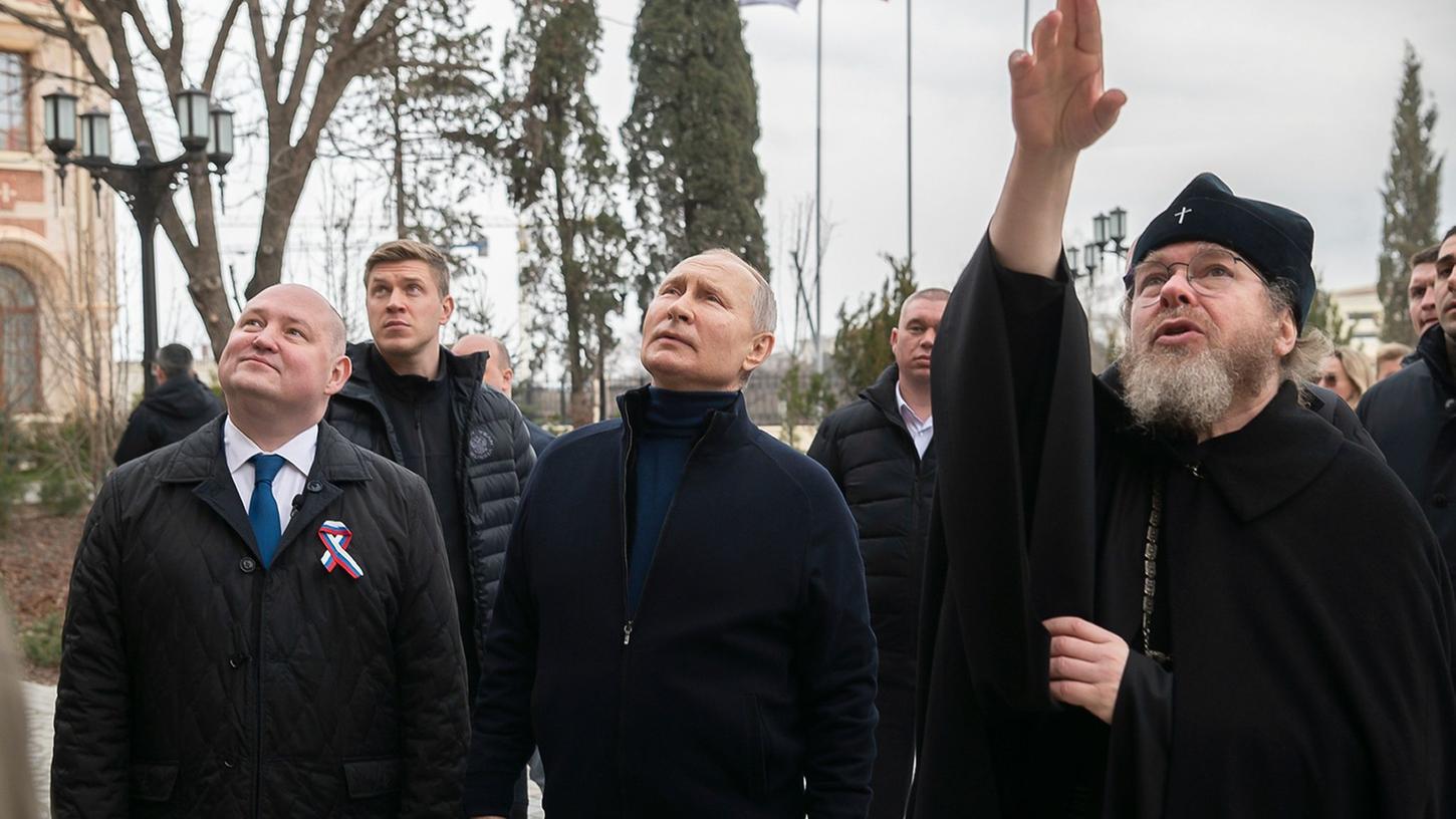 Kremlchef Putin ist zum neunten Jahrestag der russischen Annexion der Krim zu einem unangekündigten Besuch auf der Schwarzmeer-Halbinsel eingetroffen. Hier zusammen mit dem Gouverneur von Sewastopol, Michail Raswoschajew und Bischof Tichon beim Besuch einer Kunstschule für Kinder.