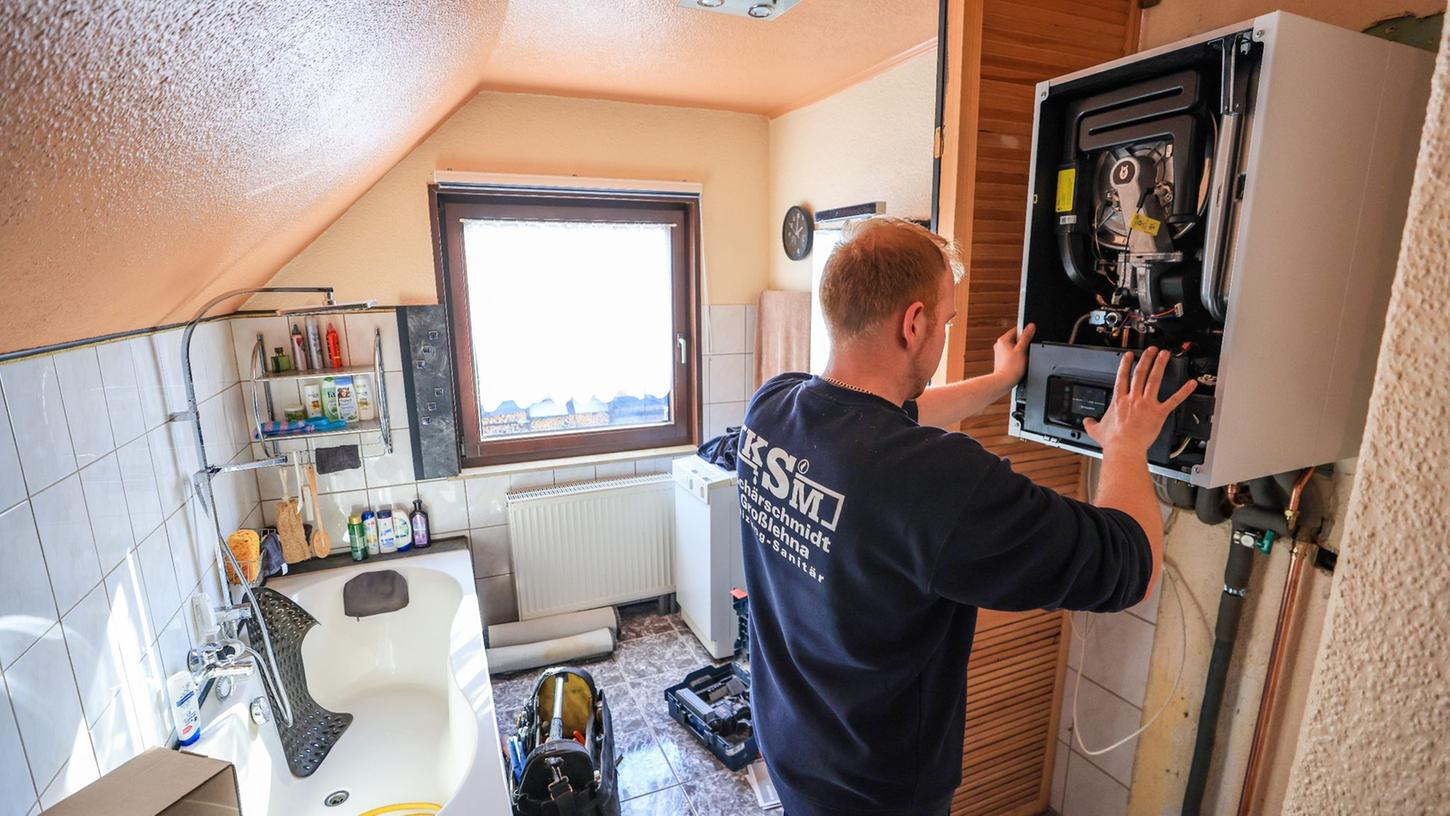 Ein Mitarbeiter einer Sanitär- und Heizungsbaufirma installiert eine moderne Gasbrennwerttherme in einem Einfamilienhaus. Ein Mitarbeiter einer Sanitär- und Heizungsbaufirma installiert eine moderne Gasbrennwerttherme in einem Einfamilienhaus.
