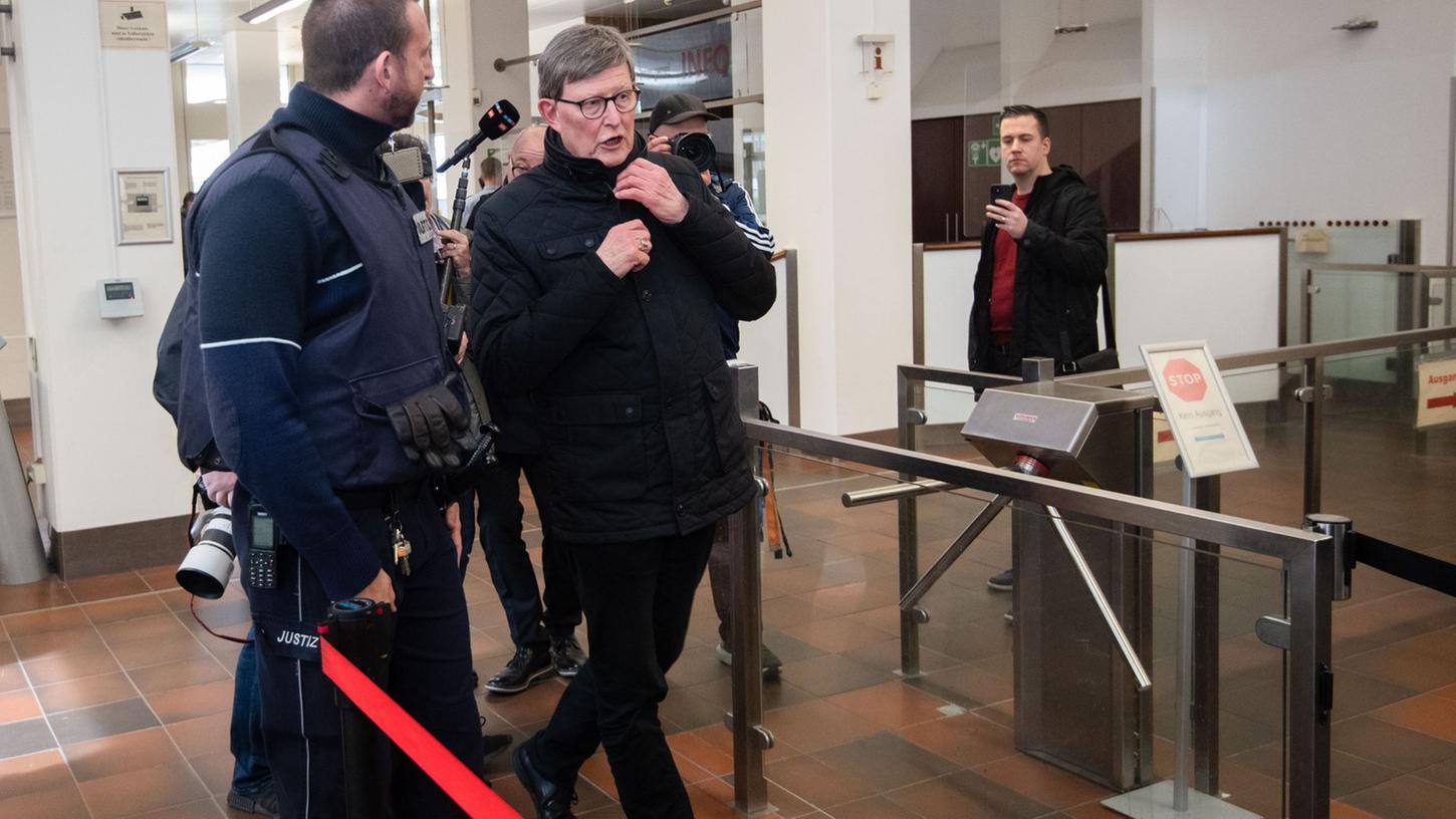 Kardinal Rainer Maria Woelki wird im Foyer des Kölner Landgerichts von einem Justizbeamten (l) zur Sicherheitsschleuse begleitet.