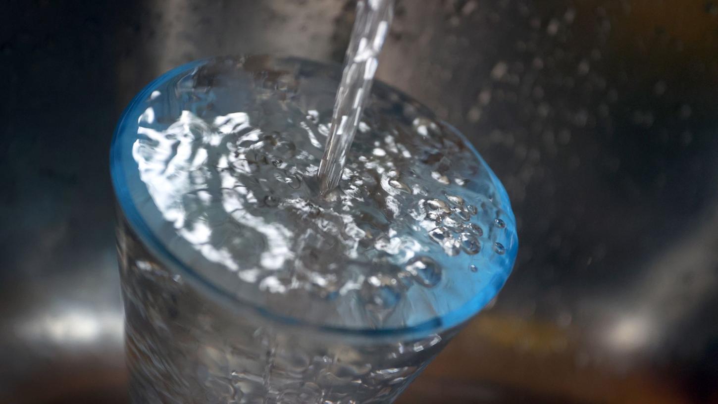 Leitungswasser fließt in ein Glas, das in einem Spülbecken steht.