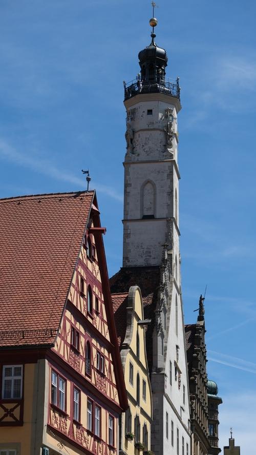 Rothenburg und seine Sehenswürdigkeiten sollte man auf jeden Fall auch von oben erkunden und dazu bieten sich zwei begehbare Türme an. Im Bild der über 60 Meter hohe Rathausturm. Da dient es zugleich der Fitness, die 220 Stufen zu erklimmen, wobei die letzten Meter eine Hühnerleiter auf die Plattform führt, die den Rundumblick auf die beeindruckende Dachlandschaft, auf Gassen und Gebäude wie die dominante Jakobskirche erlaubt. Auch auf das Taubertal, die Hohenloher Ebene im Westen und die Frankenhöhe im Osten schweift der Ausblick. So zeigt sich die Stadt immer noch eingebettet in eine herrliche Landschaft, die sich lediglich auf der Ost- und Nordseite durch moderne Siedlungsgebiete verändert hat. Weniger bekannt ist, dass man auch den Röderturm bis zum Dachstüberl erklimmen kann und von dort nochmal eine ganz andere Perspektive auf Rothenburg genießt.