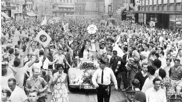 200.000 säumten am Tag nach dem achten Nürnberger Meister-Coup die Straßen in der Noris. Jung und Alt drängte sich mit Fahnen und Fotokameras bewaffnet in der Königsstraße. Die Menge ließ nur eine schmale Gasse für das Führungsfahrzeug frei. Im schicken weißen Sportflitzer sitzt der langjährige Vereinspräsident Ludwig Franz neben Nürnbergs Spielführer, der die begehrte Trophäe stolz den Massen präsentiert.