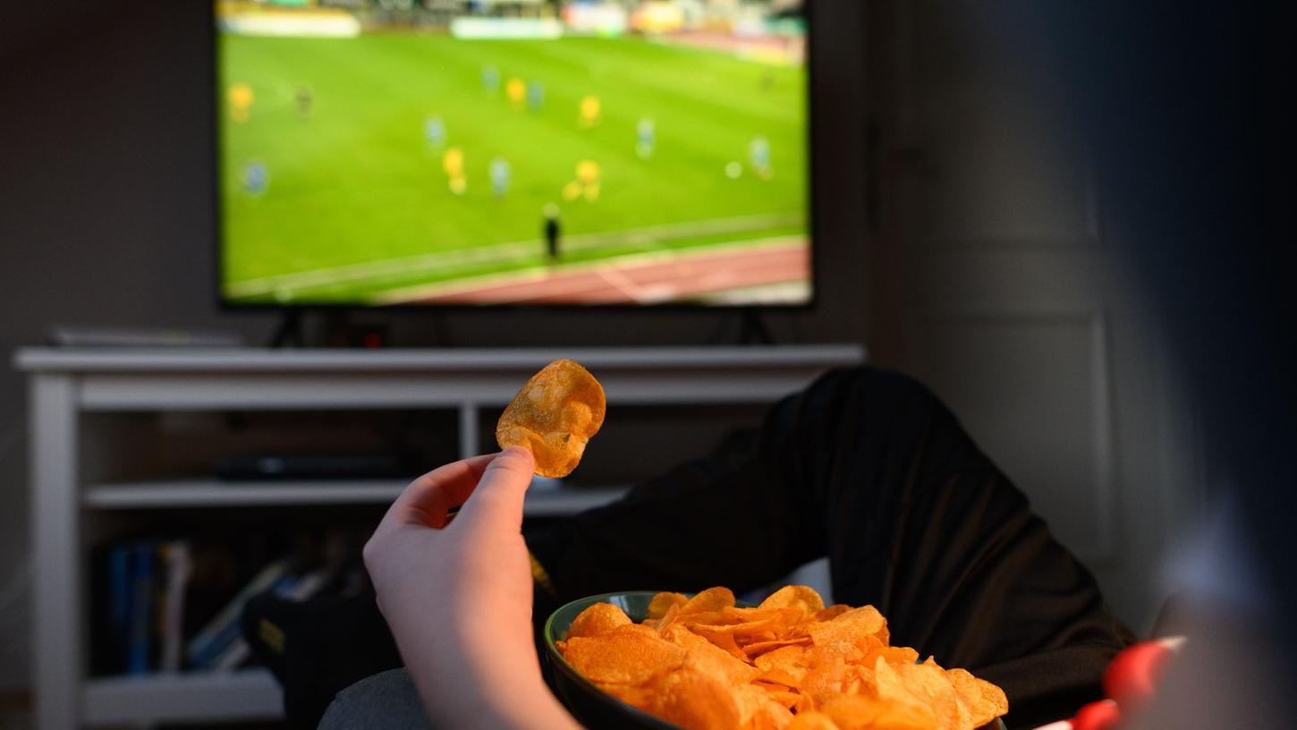 Ein Junge sitzt vor dem Fernseher und ist dabei Kartoffelchips.