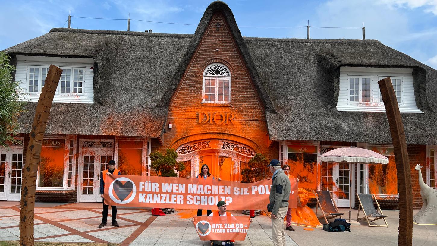 Klima-Aktivisten haben sich vor einem besprühten Luxusgeschäft auf der Insel Sylt platziert. Klima-Aktivisten haben sich vor einem besprühten Luxusgeschäft auf der Insel Sylt platziert.