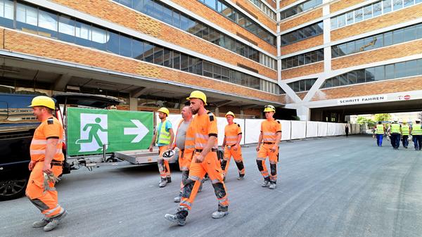 Arbeiter auf dem Weg zum Richtfest. Im früheren Versandhof wurden alle Abstellflächen für Gerät und Material sorgfältig mit Planen eingezäunt.