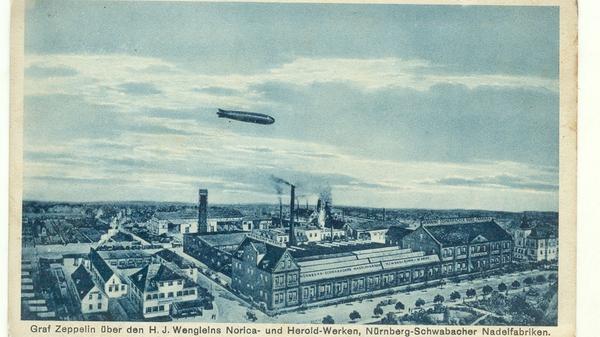 Die Nadelfabrik Wenglein machte Werbung mit dieser Postkarte vom Zeppelin-Überflug im Jahr 1909. Auf ihr sieht man das Luftschiff Graf Zeppelin über dem Werksgelände in der Bahnhofstraße (heute BayWa).