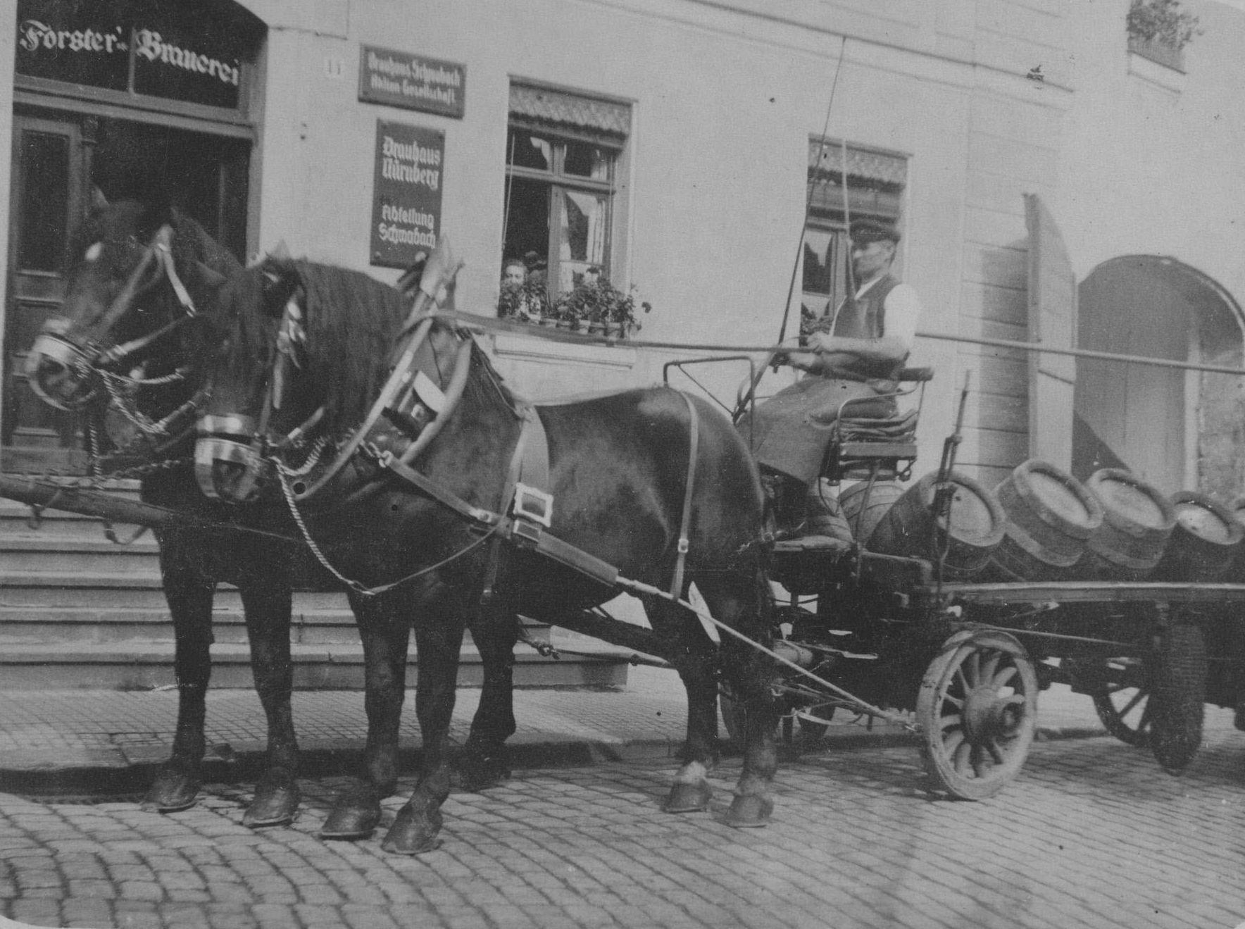 Heinrich Brechtel mit einem Bierfuhrwerk vor dem Anwesen Hördlertorstraße 14. Er war über 40 Jahre lang zunächst im landwirtschaftlichen Betrieb und später als Bierkutscher für die Schwabacher Forster-Brauerei tätig. Das Foto entstand um 1928. Aus dem Fenster schaut die Haushälterin von Julius Forster. Die Schilder am Haus geben einen Großteil der Geschichte wieder. Über der Tür steht "Forster-Brauerei", rechts daneben "Brauhaus Schwabach. Aktien-Gesellschaft", darunter hängt schließlich ein Schild mit der Aufschrift "Brauhaus Nürnberg, Abteilung Schwabach".