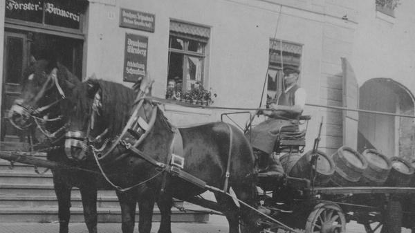 Heinrich Brechtel mit einem Bierfuhrwerk vor dem Anwesen Hördlertorstraße 14. Er war über 40 Jahre lang zunächst im landwirtschaftlichen Betrieb und später als Bierkutscher für die Schwabacher Forster-Brauerei tätig. Das Foto entstand um 1928. Aus dem Fenster schaut die Haushälterin von Julius Forster. Die Schilder am Haus geben einen Großteil der Geschichte wieder. Über der Tür steht "Forster-Brauerei", rechts daneben "Brauhaus Schwabach. Aktien-Gesellschaft", darunter hängt schließlich ein Schild mit der Aufschrift "Brauhaus Nürnberg, Abteilung Schwabach".