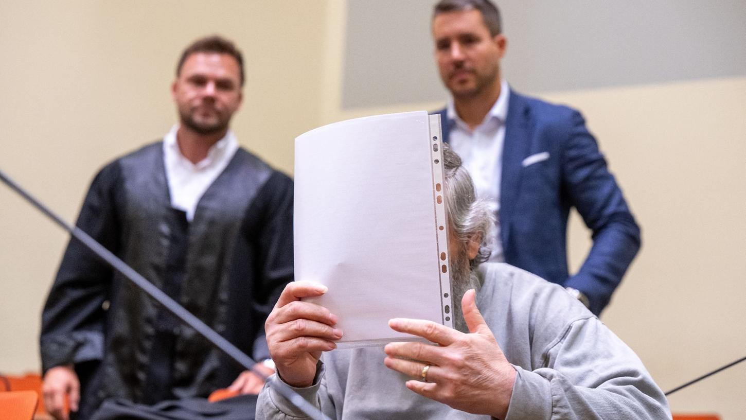 Der Angeklagte hält sich im Gerichtssaal ein Blatt Papier vor das Gesicht. Im Hintergrund stehen seine Anwälte.