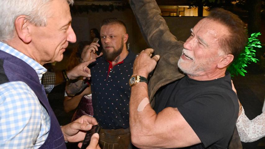Der Wirt des Marstallzelts Siegfried Able (l) spricht dem Schauspieler Arnold Schwarzenegger, der gerade seine Jacke anzieht.
