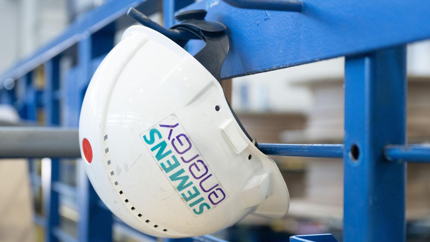 Ein Schutzhelm mit der Aufschrift "Siemens Energy" hängt in einer Werkhalle.