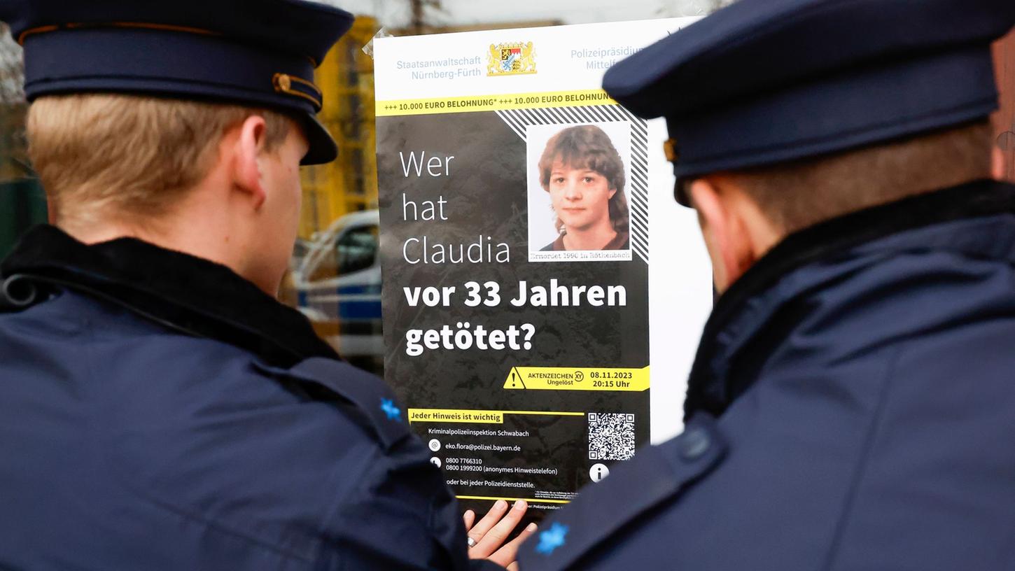 Polizisten hängen das Plakat zum Cold Case von Claudia Obermeier an einer Glasscheibe auf.