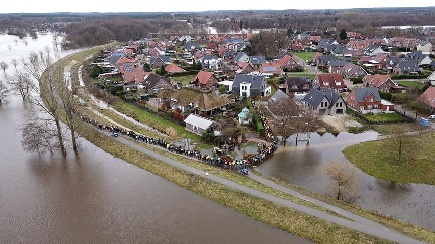 Einsatzkräfte und Einwohner sichern mit einer Menschenkette gemeinsam einen durchweichten Deich im Landkreis Emsland.