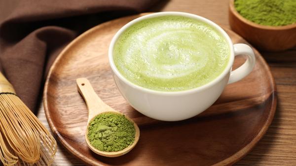 Cup of fresh matcha latte and powder on wooden table