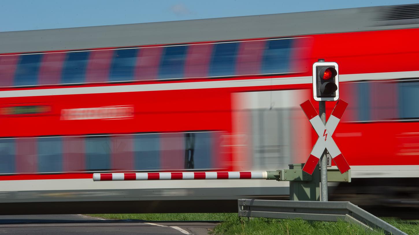 Symbolbild: Ein Regionalexpress fährt an einem geschlossenem Bahnübergang vorbei.