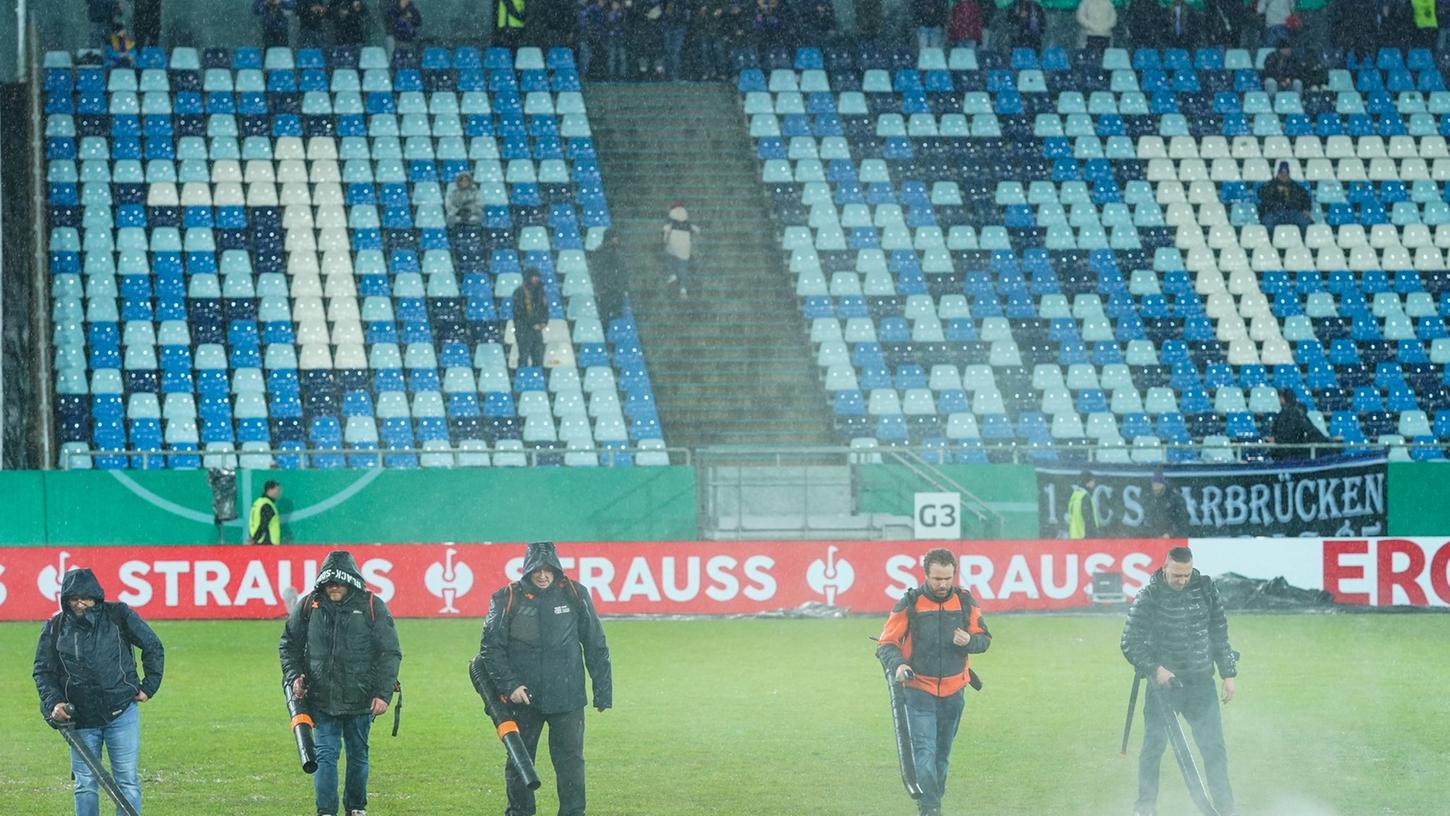 Im Ludwigspark-Stadion versuchen Helfer, Wasserlachen vom Spielfeld zu entfernen.