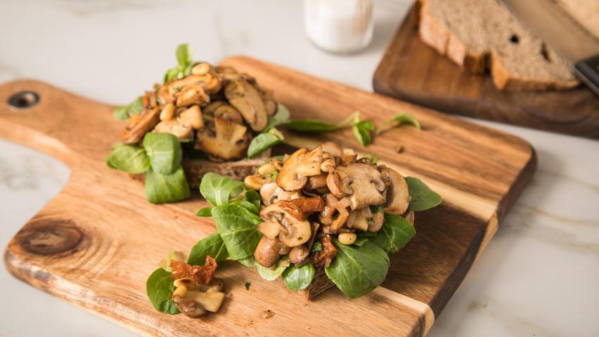 Pilze werden als natürlicher Fleischersatz immer populärer. Statt einer Wurststulle, kann man die Brotscheibe auch mit Champignons, getrockneten Tomaten und Feldsalat belegen.
