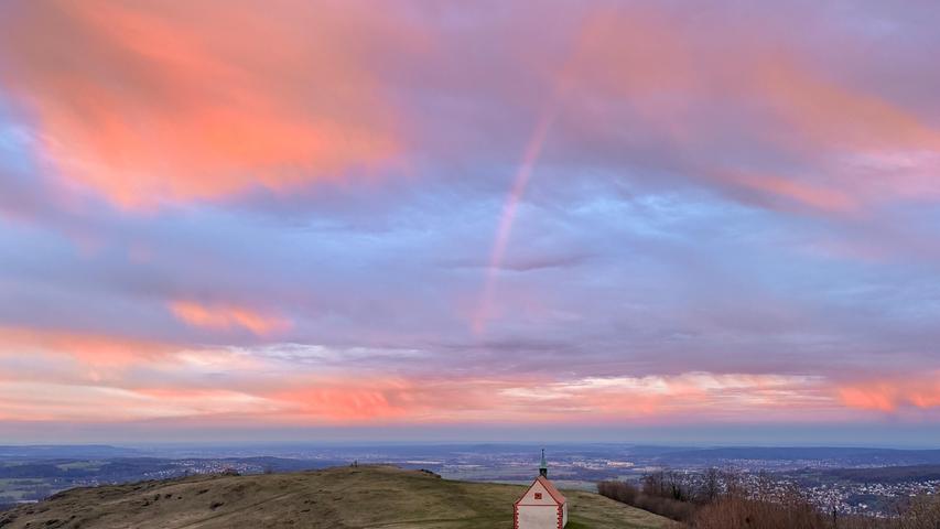 Ein farbenfroher Morgenhimmel mit Regenbogen entfaltet sich über der Walburgiskapelle auf dem Walberla. Mehr Leserfotos finden Sie hier