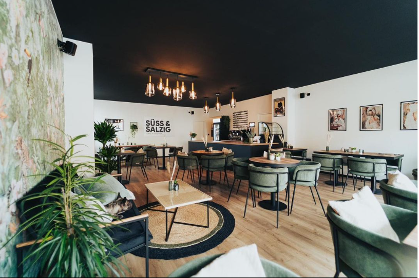 Die Einrichtung folgt einer ganz bestimmten Logik: Eine grüne Tapete mit Pflanzenmuster trifft auf Rattan-Teppich, grüne Samt-Sessel auf helle Holzmöbel, exotische Zimmerpflanzen auf ein Schild mit der Aufschrift "More Espresso, less depresso".