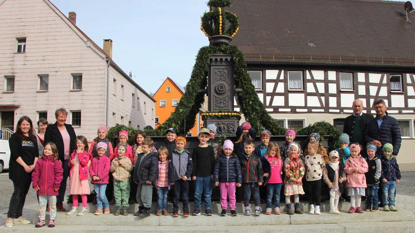 Die Heidenheimer Kindergarten-Kinder mit Bürgermeisterin Susanne Feller sowie dem 2.Bürgermeister Gerhard Neumeyer und Pfarrer Johannes Heidecker zeigen voller Stolz ihren hübschen Osterbrunnen.
