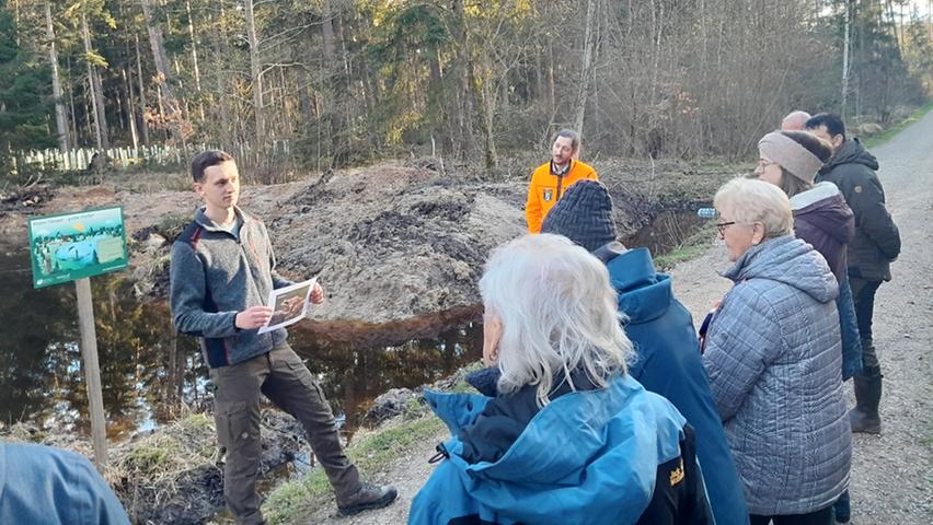 Forstanwärter Markus Täufer erläutert die Vorteile des neu angelegten Feuchtbiotops in Bezug auf den Wasserrückhalt und Artenschutz im Wald. Im Hintergrund zu sehen ist Richard Kral vom Amt für Ernährung, Landwirtschaft und Forsten Roth-Weißenburg.