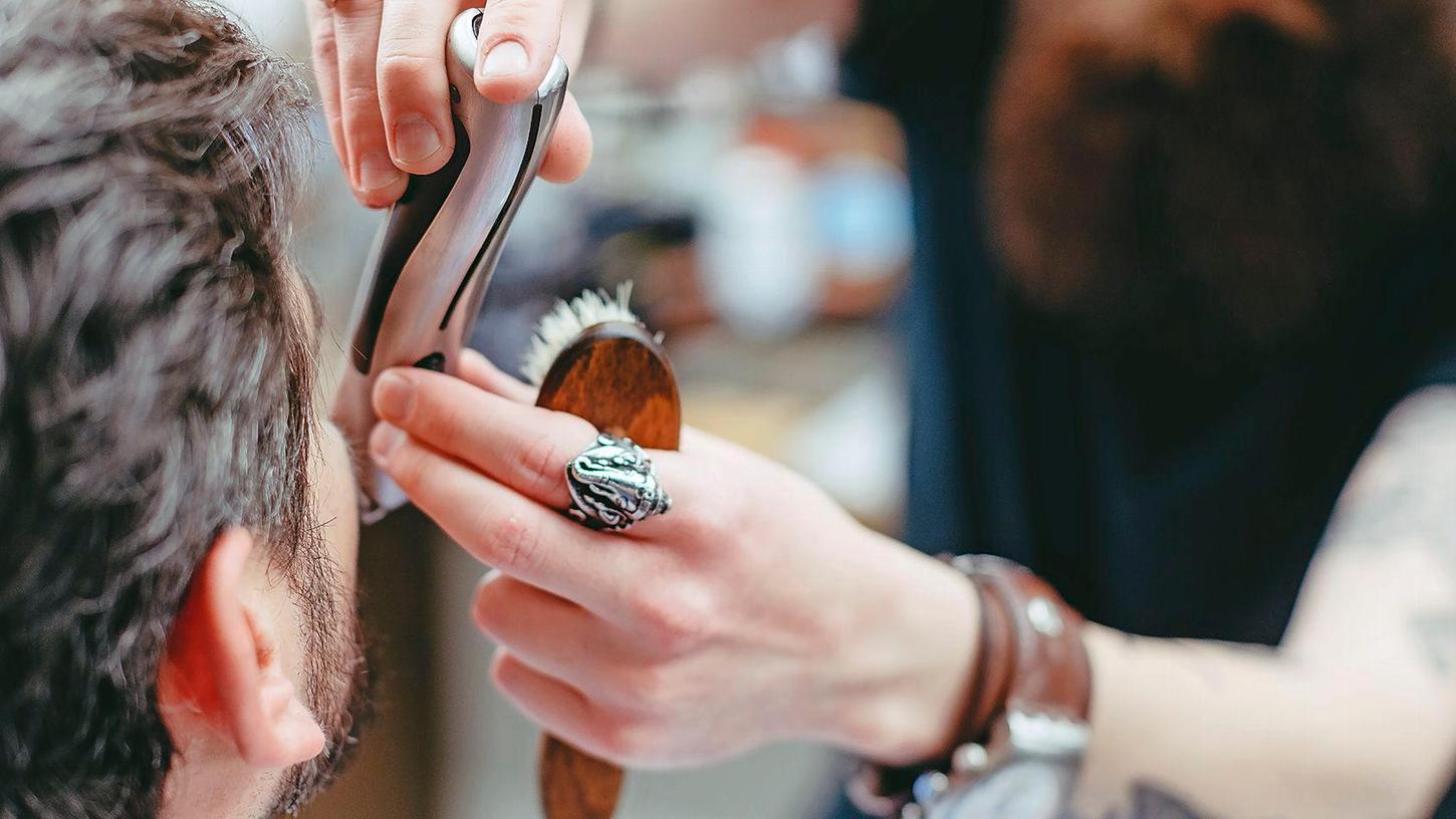 Ein Friseur schneidet einem Kunden den Bart.