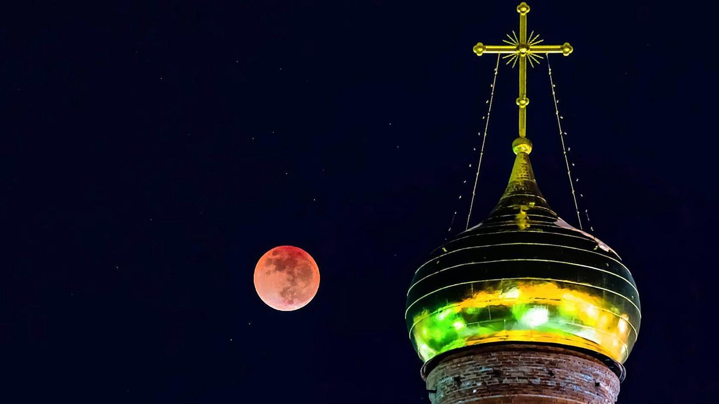 Dom einer Kirche bei Nacht vor rotem Mond. (Symbolbild)