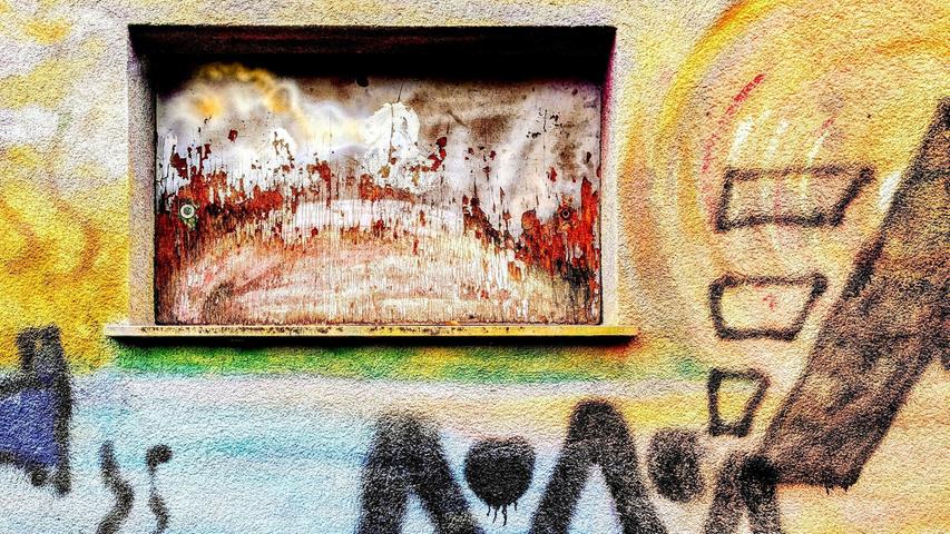 Eine oxidierte Metallplatte im Fenster sowie Graffiti an der Hausfassade der BRK Wasserwacht-Station Kleiner Dutzendteich. Unserer Leserfotografin Hildegard Preis stellt sich folgende Frage: Wer malt die schöneren Bilder, die Natur oder der Mensch?