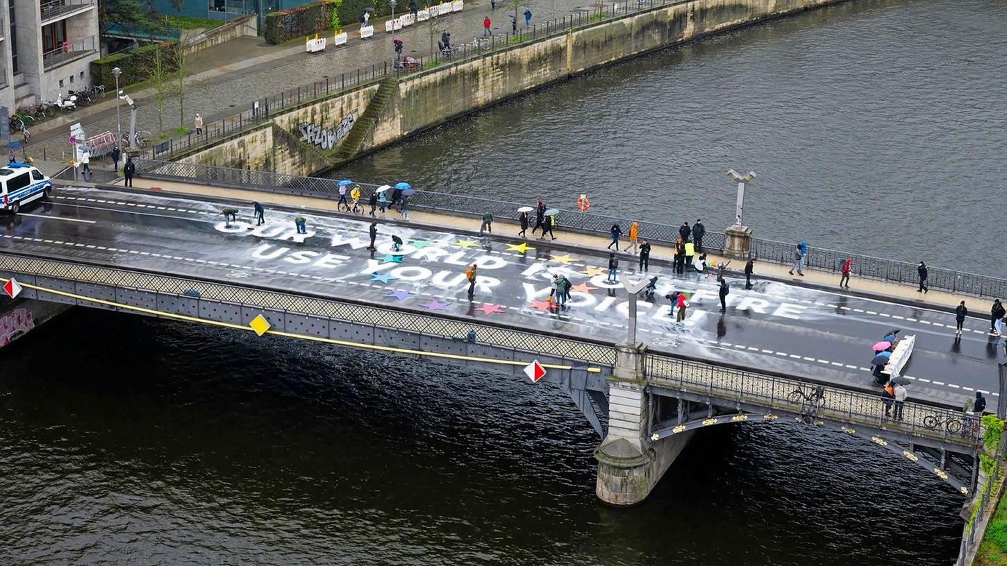 Klimaaktivisten der Bewegung Fridays for Future malen auf der Marschallbrücke in Berlin den Schriftzug "Our world is on fire - use your voice!".