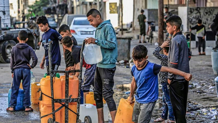 Palästinensische Kinder stehen mit Wasserbehältern Schlange, um sie mit Trinkwasser zu füllen.