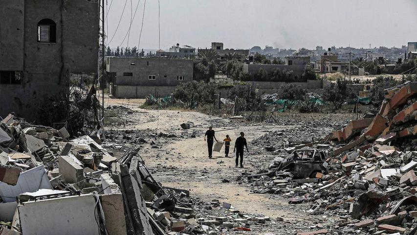 Palästinenser gehen neben zerstörten Wohngebäuden im Lager Nuseirat im zentralen Gazastreifen entlang.