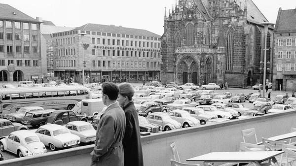 Von einer Caféterrasse aus blickt ein Paar im Jahr 1965 auf ein Meer aus Fahrzeugen, das den Hauptmarkt flutet. Trotz der Wetterkapriolen nutzten viele Touristen die freien Ostertage, um Nürnbergs Sehenswürdigkeiten zu besichtigen, auch Theateraufführungen oder die Auschwitz-Ausstellung im Rathaus standen bei vielen auf dem Programm. An Sonntagen durfte die „gute Stube“ Nürnbergs seinerzeit als Parkplatz genutzt werden. Noch bis in die 1980er Jahre gab es an der Südseite des Hauptmarkts 40 Stellplätze, ehe auch diese auf Beschluss des Stadtrats im Jahr 1982 Teil der Fußgängerzone wurden.