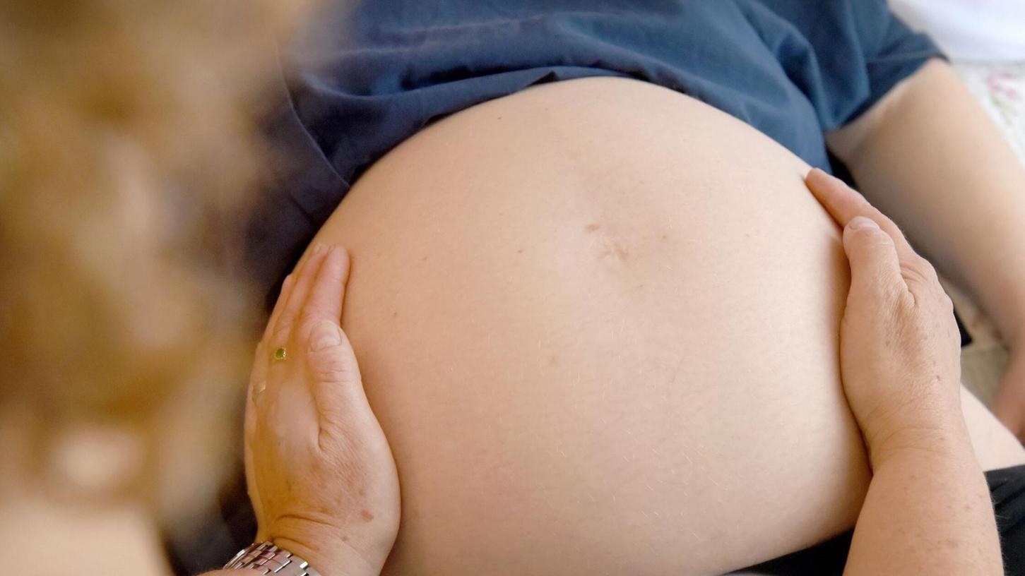 Eine Hebamme tastet den Bauch einer Frau ab, die im neunten Monat schwanger ist.