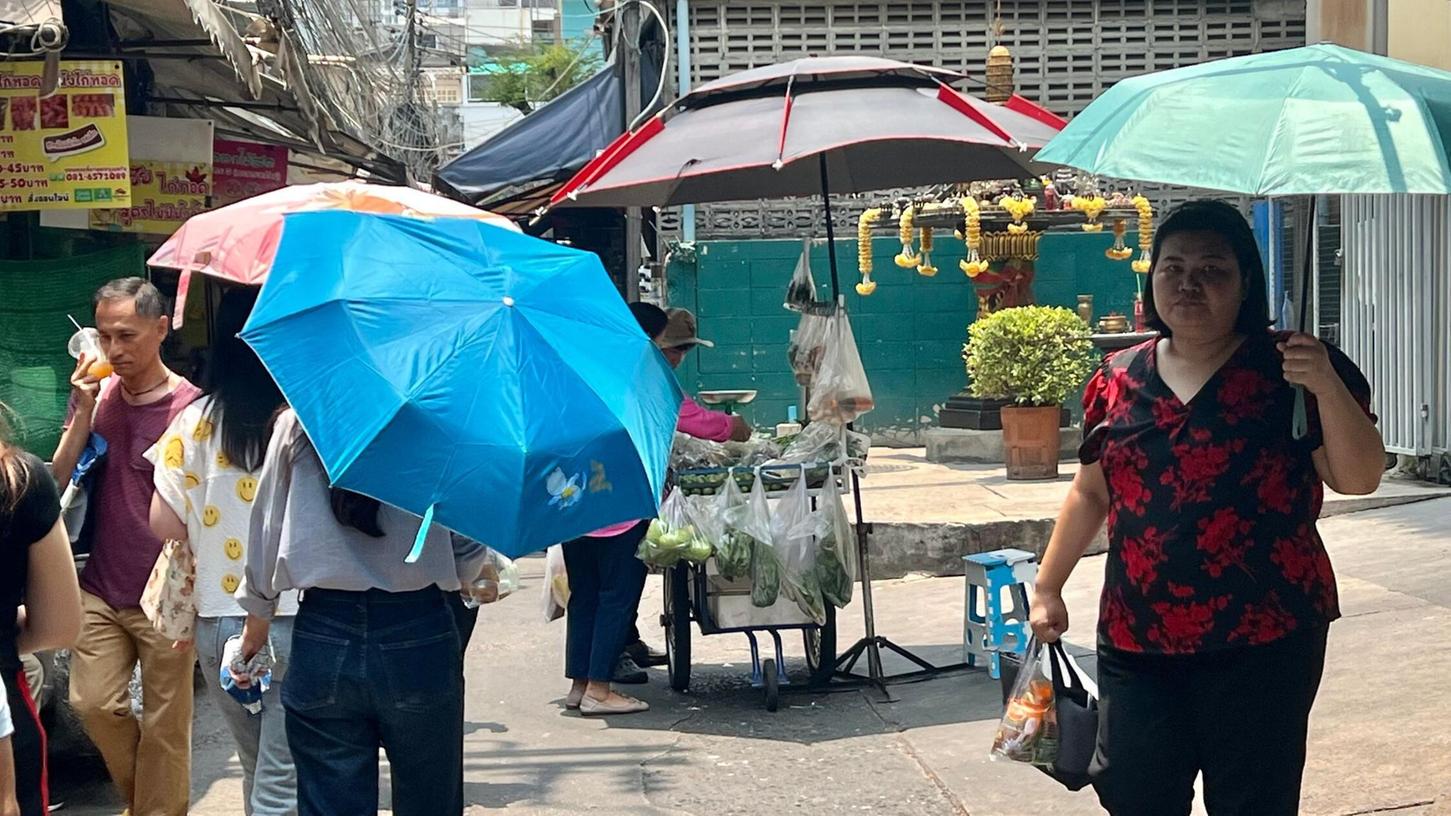 Menschen schützen sich in Bangkok mit Schirmen vor der extremen Hitze und vor der Sonne.
