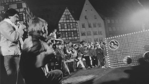 Am 1. Dezember 1984 stand der Tiergärtnertorplatz ganz im Zeichen des Fußballs: Das ZDF-Sportstudio gastierte mit seiner Torwand in Nürnberg. Nachdem sich eine Stunde lang die Kinder an der Wand probieren durften (unser Foto), wurde es ernst: Unter über 100 Teilnehmern galt es, den besten für das Duell mit dem damaligen HSV-Spieler Felix Magath herauszufinden. Im Stechen qualifizierte sich schließlich der 16jährige Oliver Schwan vom VfL Nürnberg mit vier Treffern. Als er dann live gegen Magath antreten durfte, schoss er den Ball noch zweimal erfolgreich durch die Torwand, was ihm überraschenderweise den Sieg bescherte.