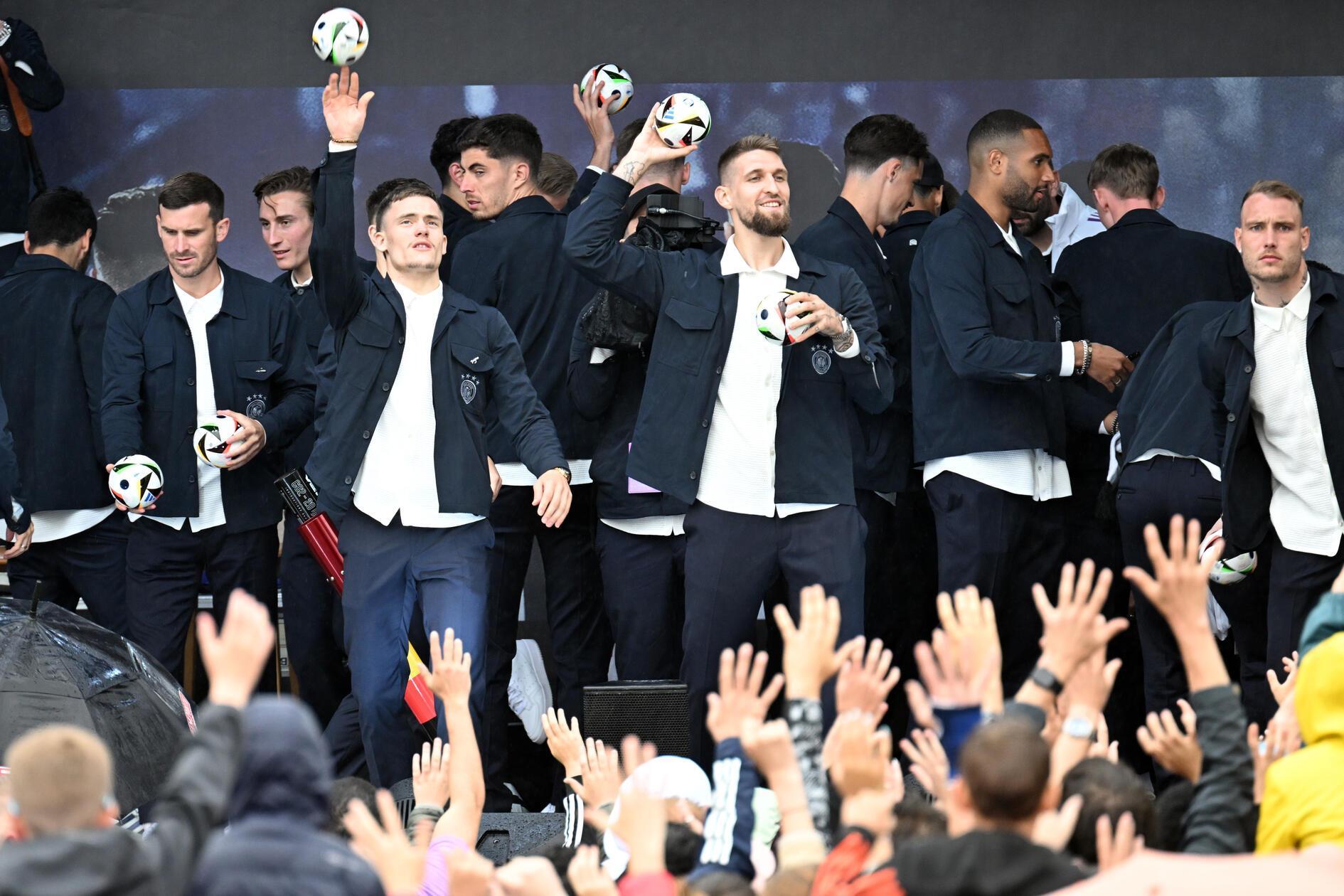 Die Nationalmannschaft steht auf der Bühne. Florian Wirtz (Mitte l.) und Robert Andrich (Mitte) werfen kleine Fußbälle in die Zuschauermenge.