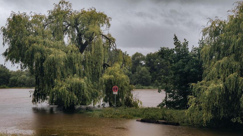 Schilder und Parkplätze am Ufer sind überflutet, der Fluss bahnt sich seinen Weg.